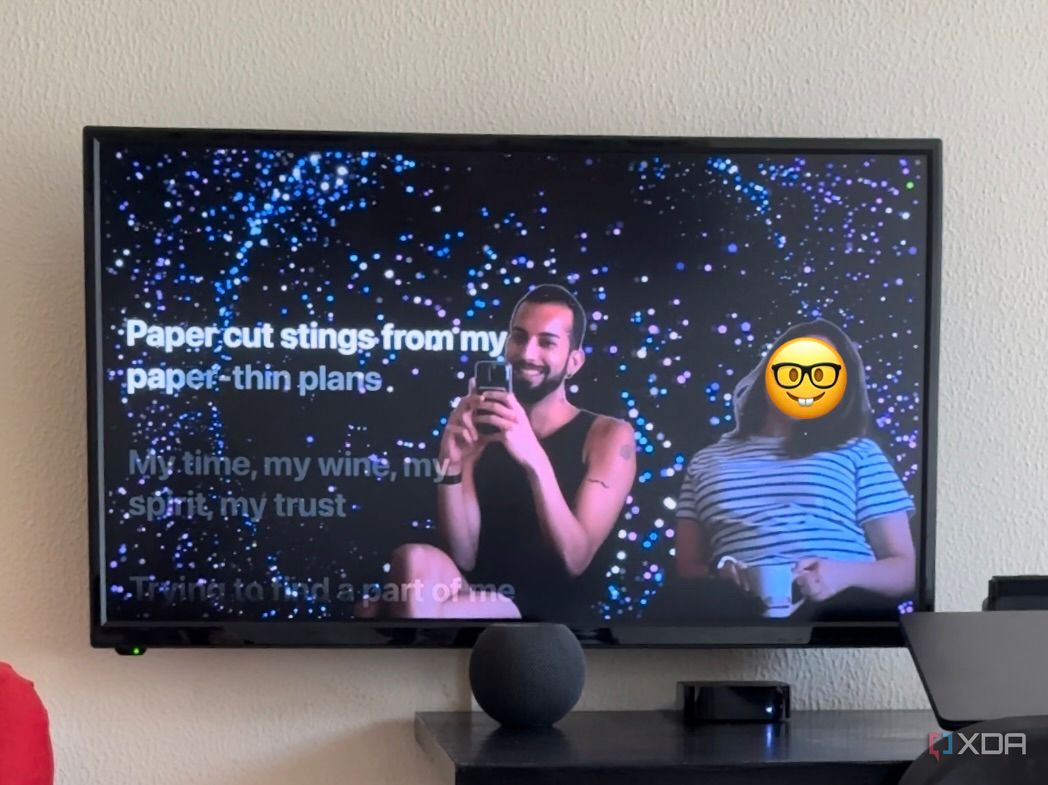 Mahmoud Itani y otra persona que aparecen en la pantalla del televisor junto a las letras de Apple Music con efectos especiales aplicados