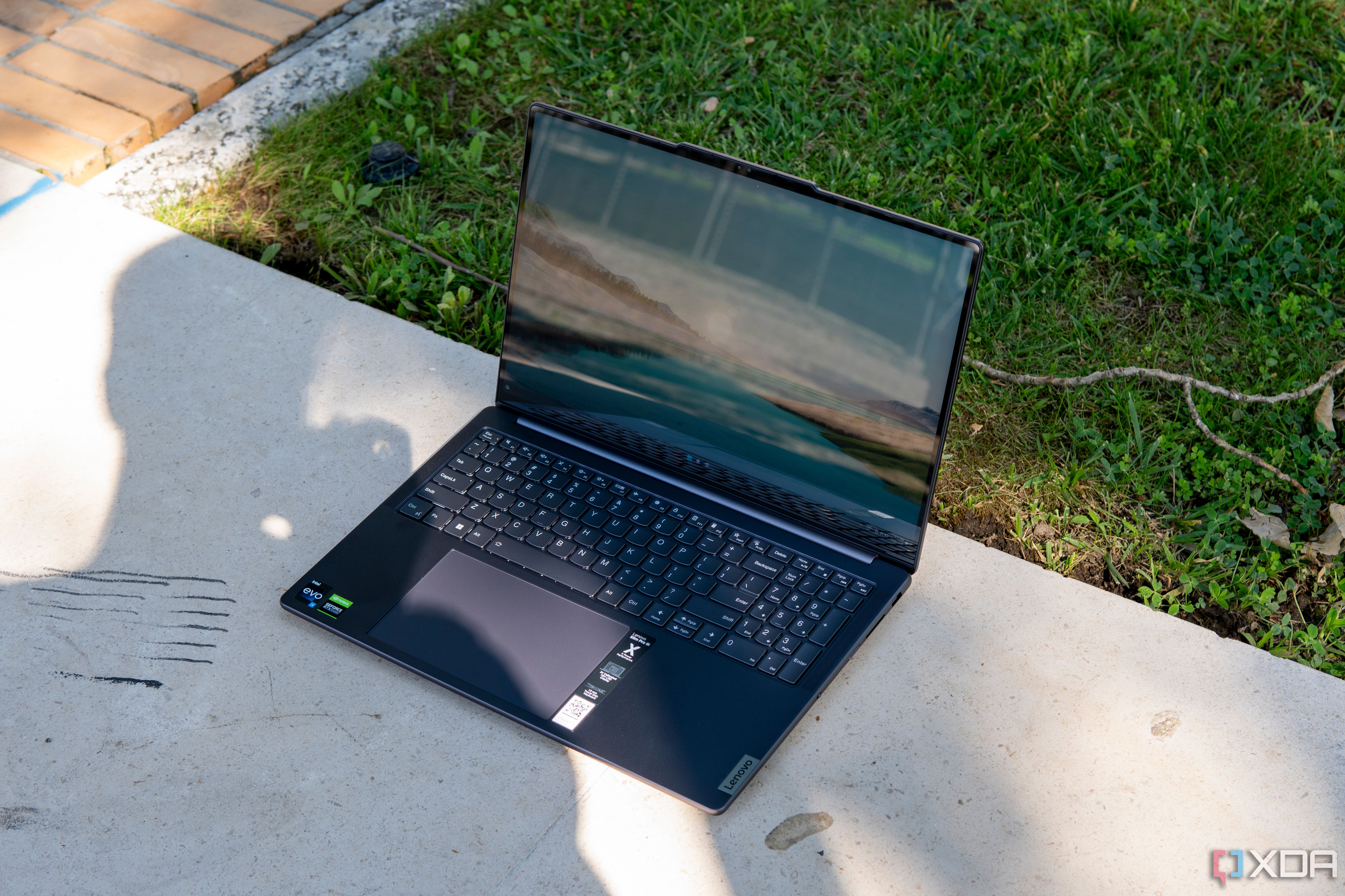 Angled view of the Lenovo Slim Pro 9i 16-inch model on a large flat stone with grass in the background