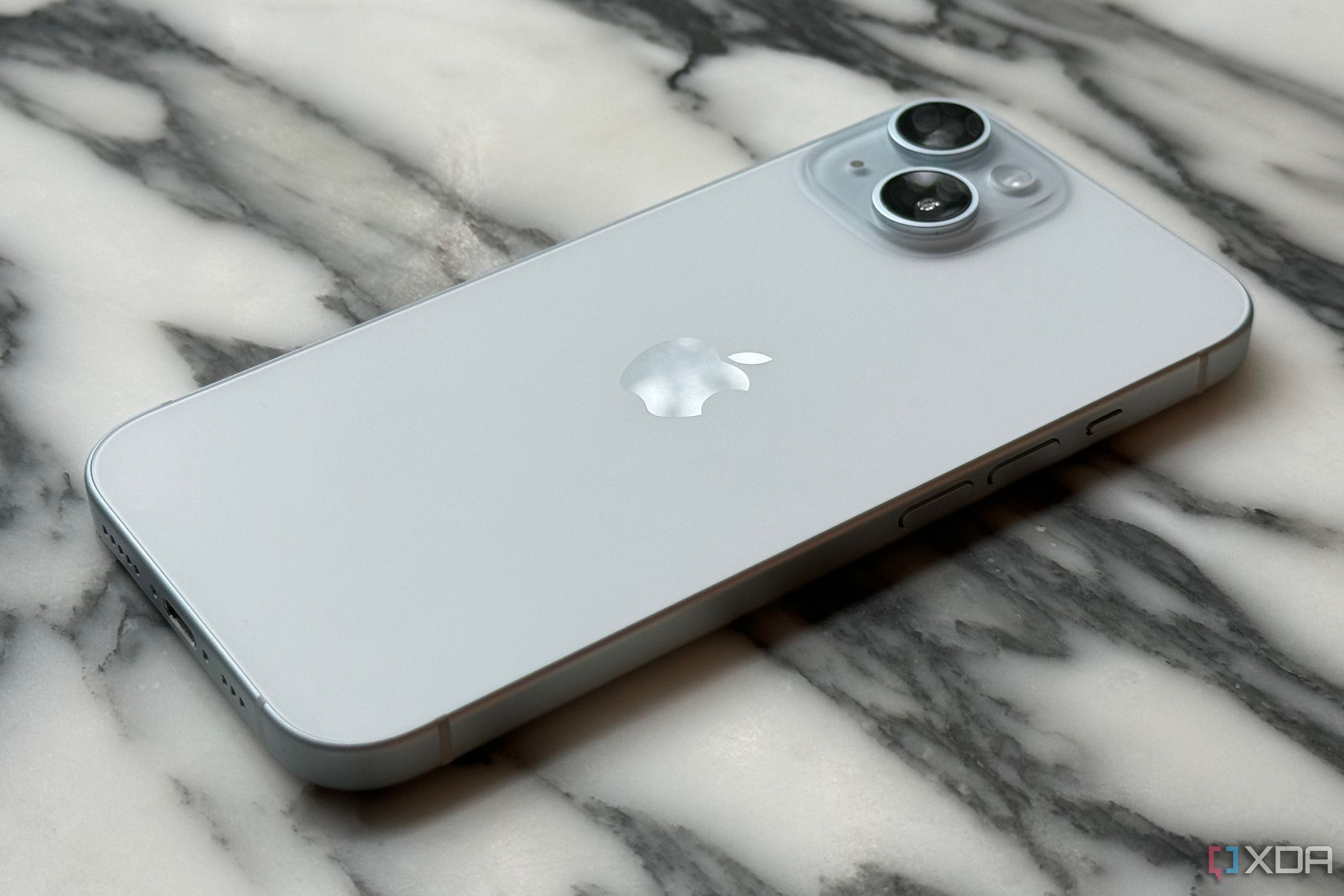 A blue iPhone 15 resting on a marble tabletop.