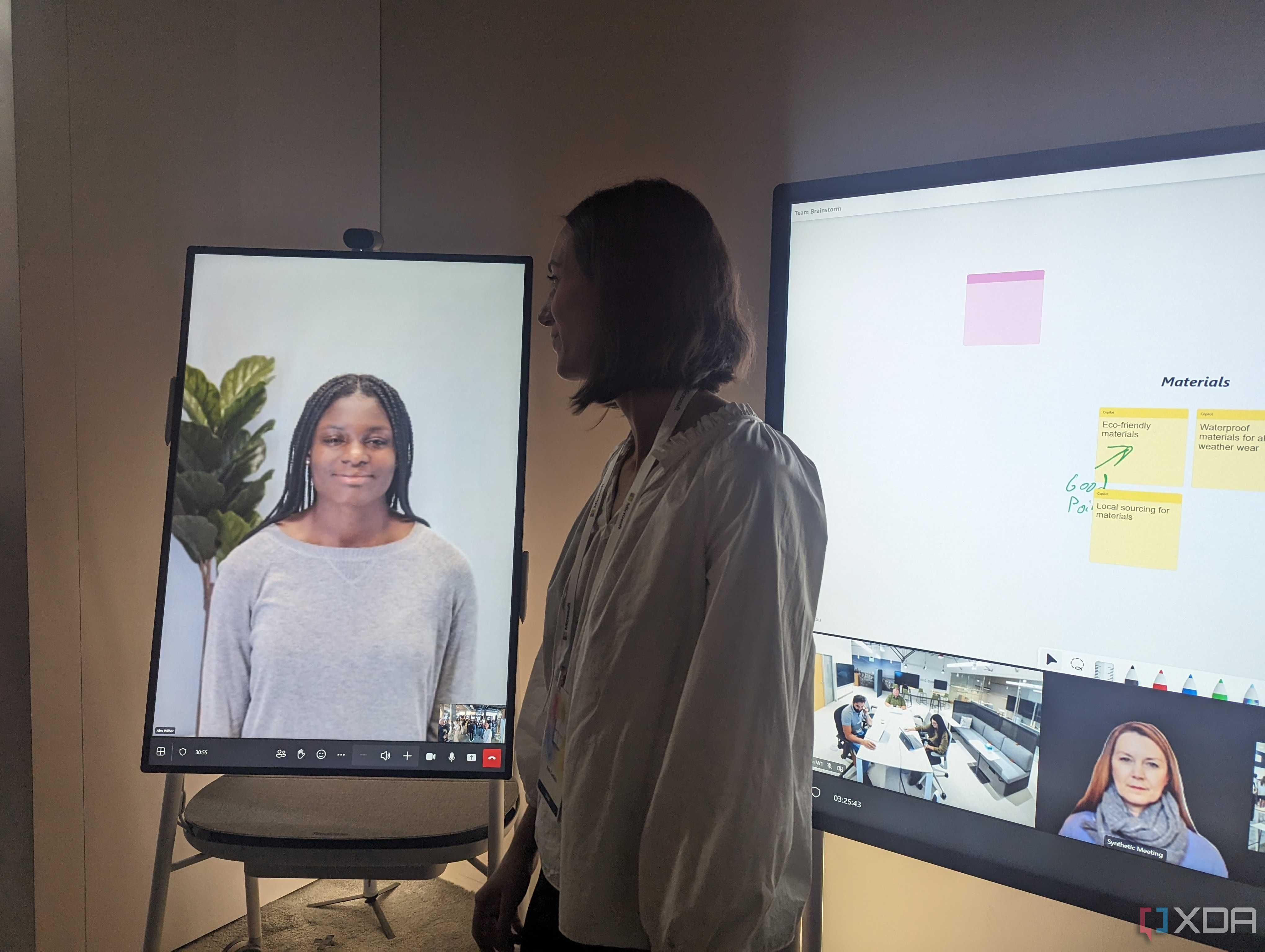 Женщина стоит между двумя устройствами Surface Hub, на одном из которых отображается экран вызова, а на другом — доска.