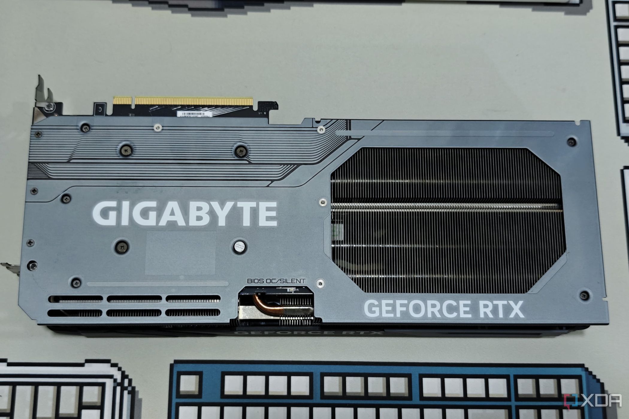 Изображение задней панели графического процессора Gigabyte GeForce RTX 4070 Ti Gaming OC, стоящего на подставке под столом.