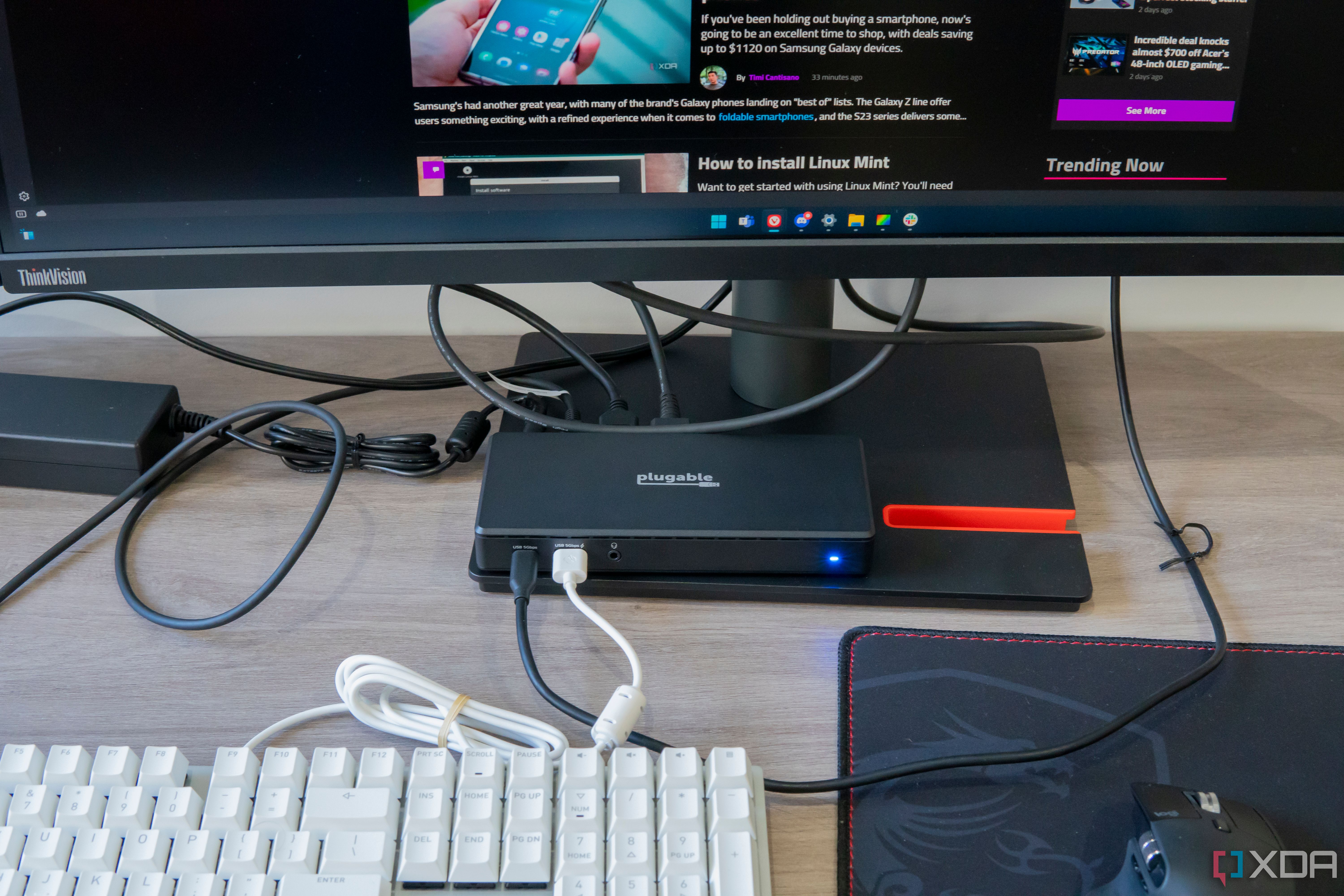 A Plugable dock connected to multiple peripherals on a desk, including a keyboard, mouse, and monitor