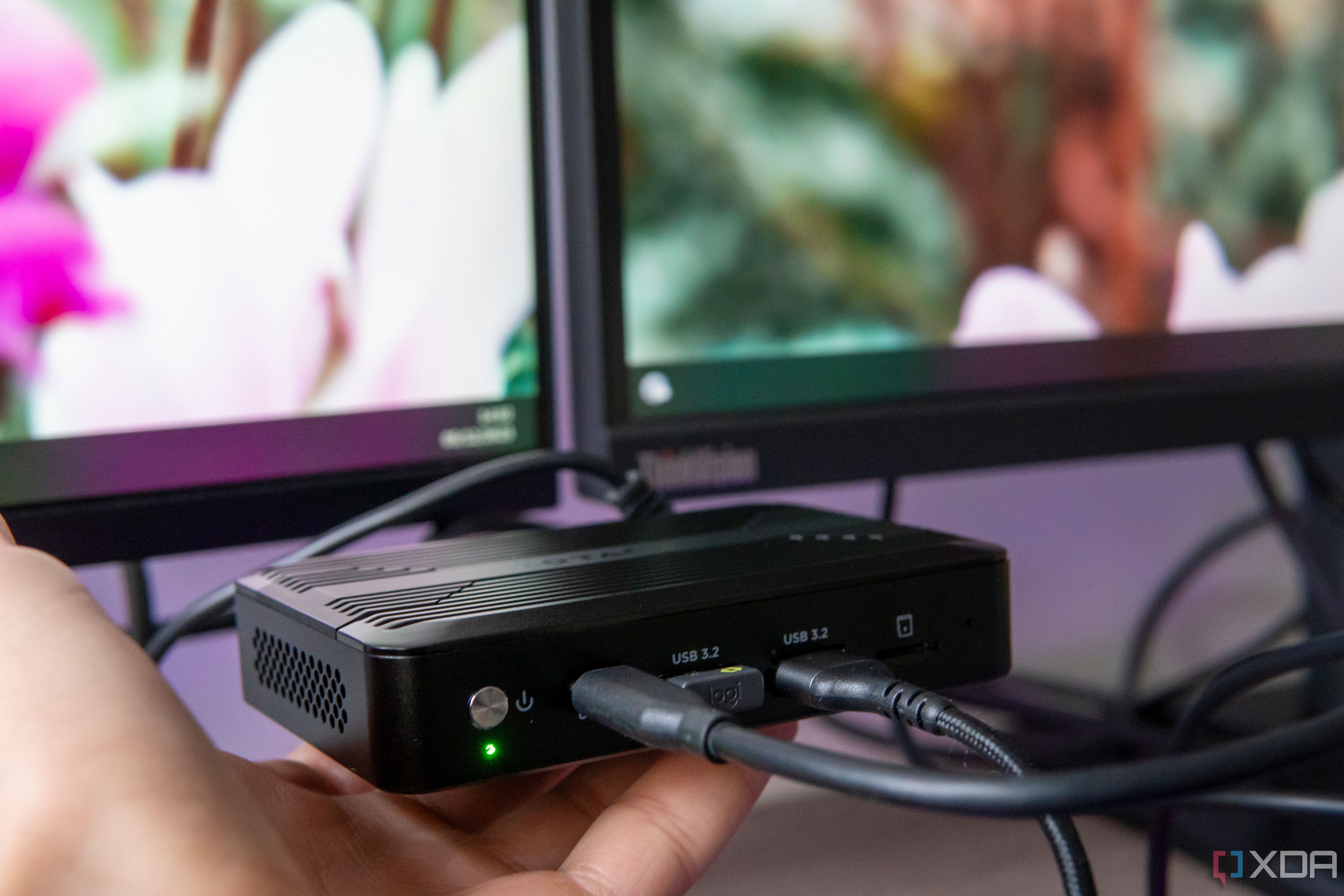 Angled view of the Zotac Zbox Pico PI430AJ on someone's hand in front of two monitors