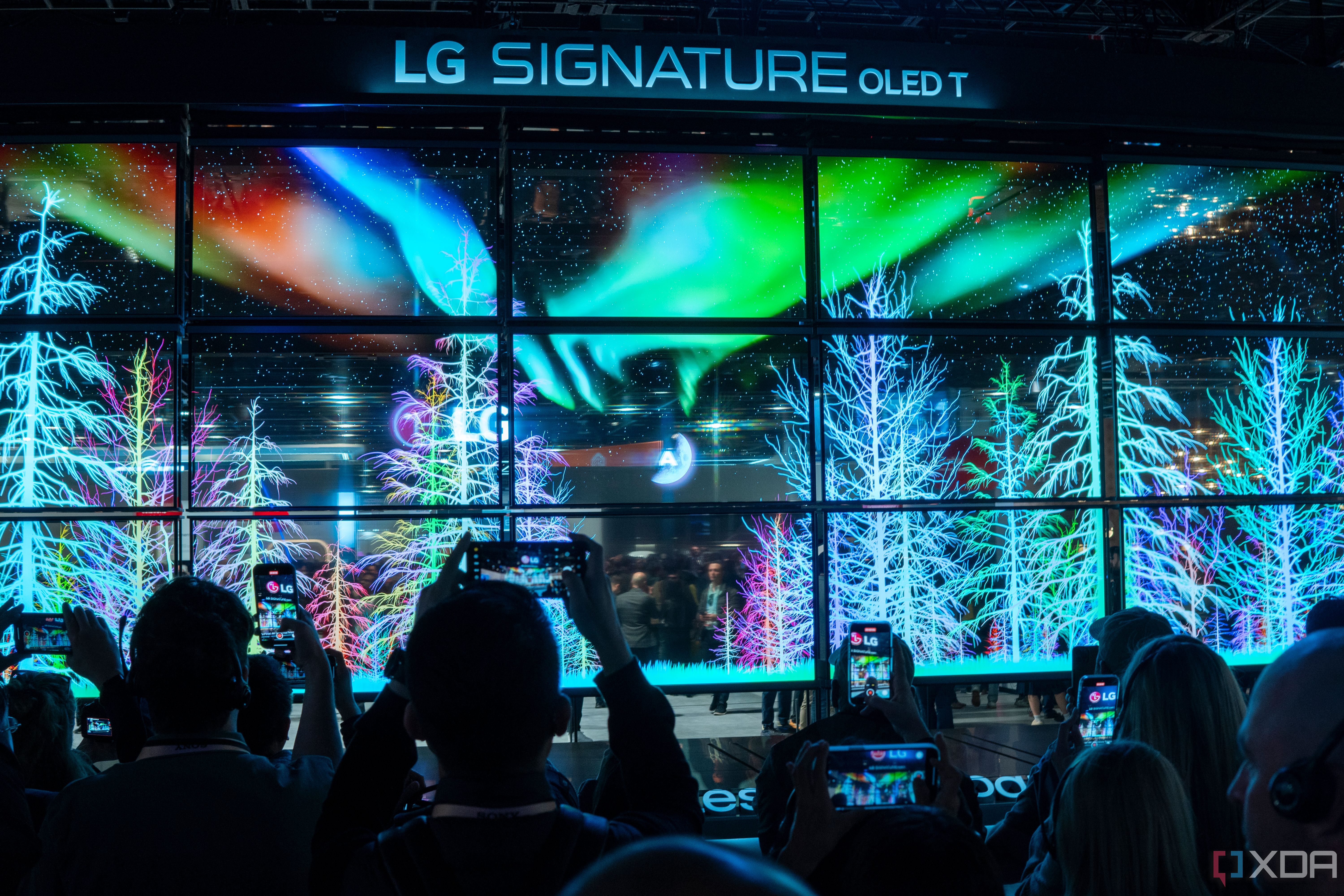 A wall of transparent LG OLED TVs showing a colorful forest with lights in the night sky