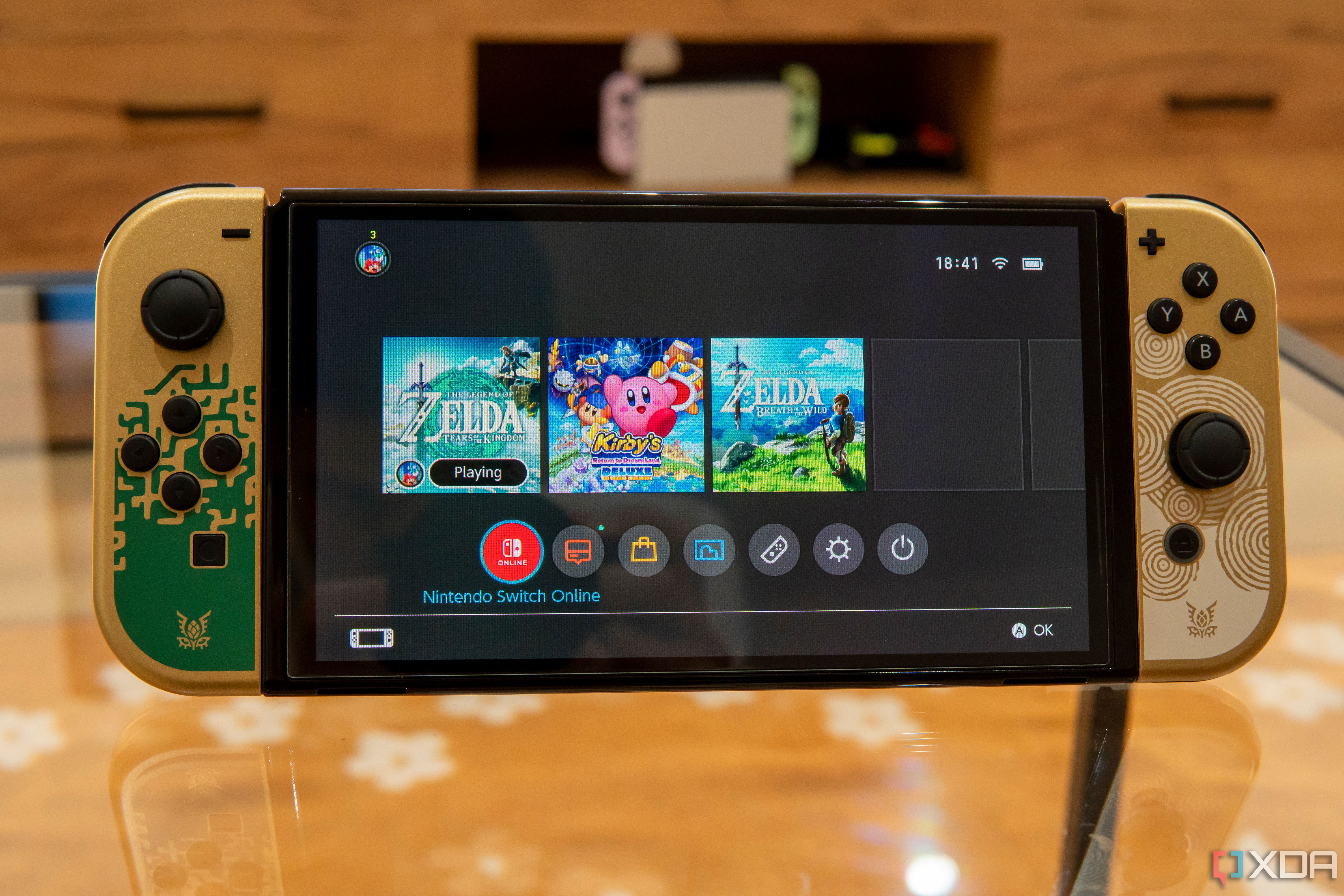Front view of the Nintendo Switch OLED model displaying the Home menu with a game running in the background