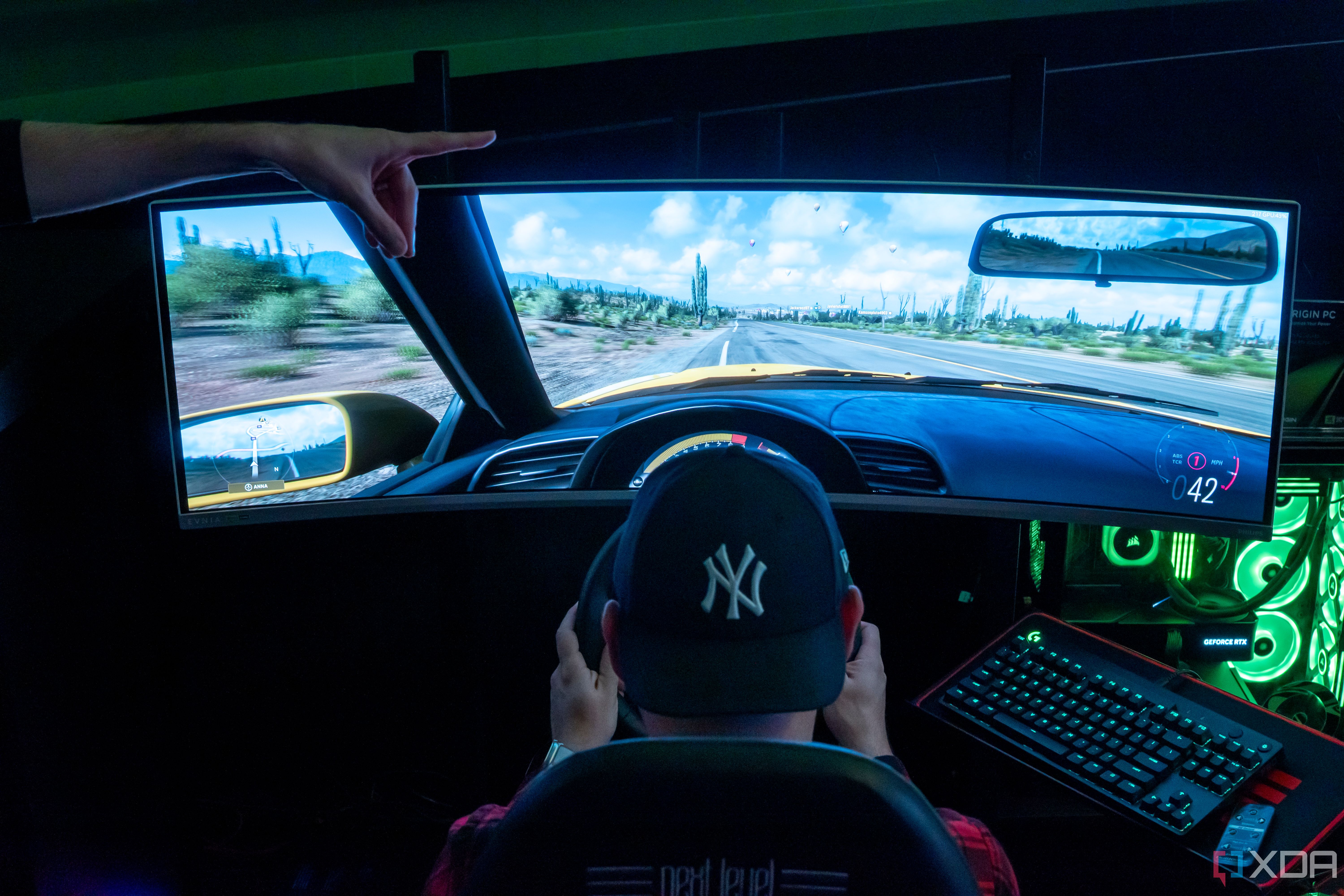 A man sitting in a gaming chair and using a steering wheel to play a videogame on a large monitor