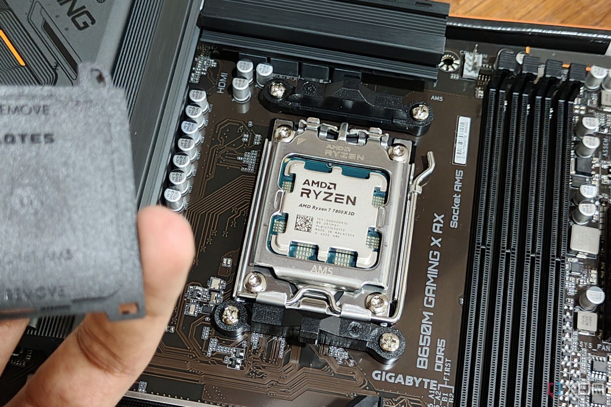 Изображение процессора AMD Ryzen 7 7800X3D, установленного на материнской плате, с человеком на переднем плане, держащим в руке крышку разъема.