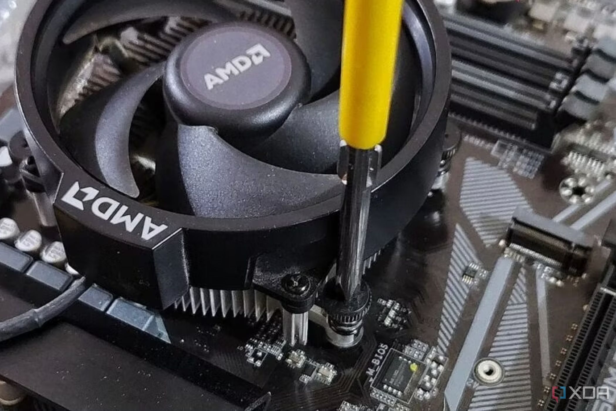 An image showing a stock AMD cooler being screwed to the motherboard using a screwdriver.