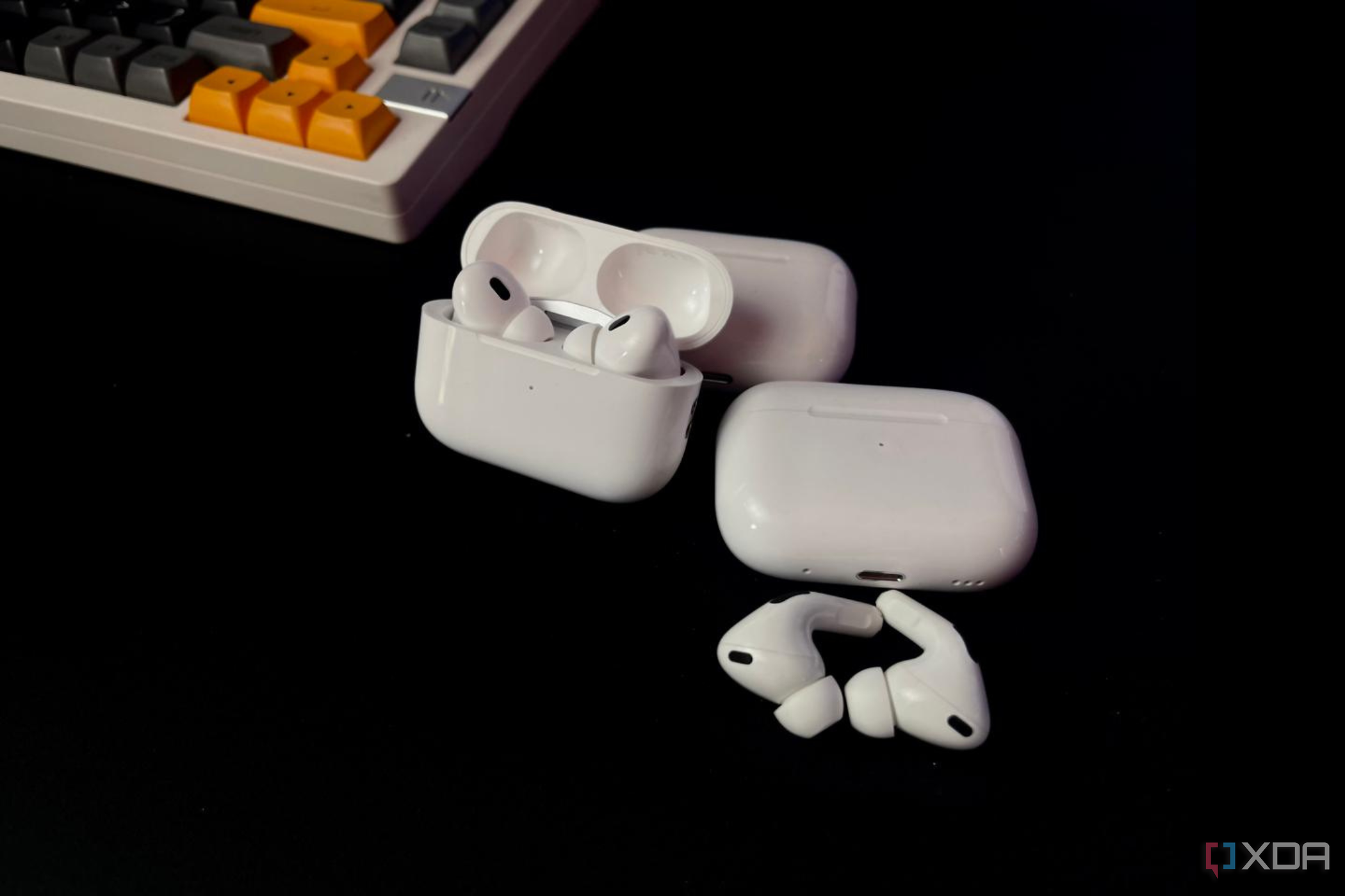 Image of a pair of AirPods Pro with an open charging case on a black background next to a Zuoya LMK81 mechanical keyboard.