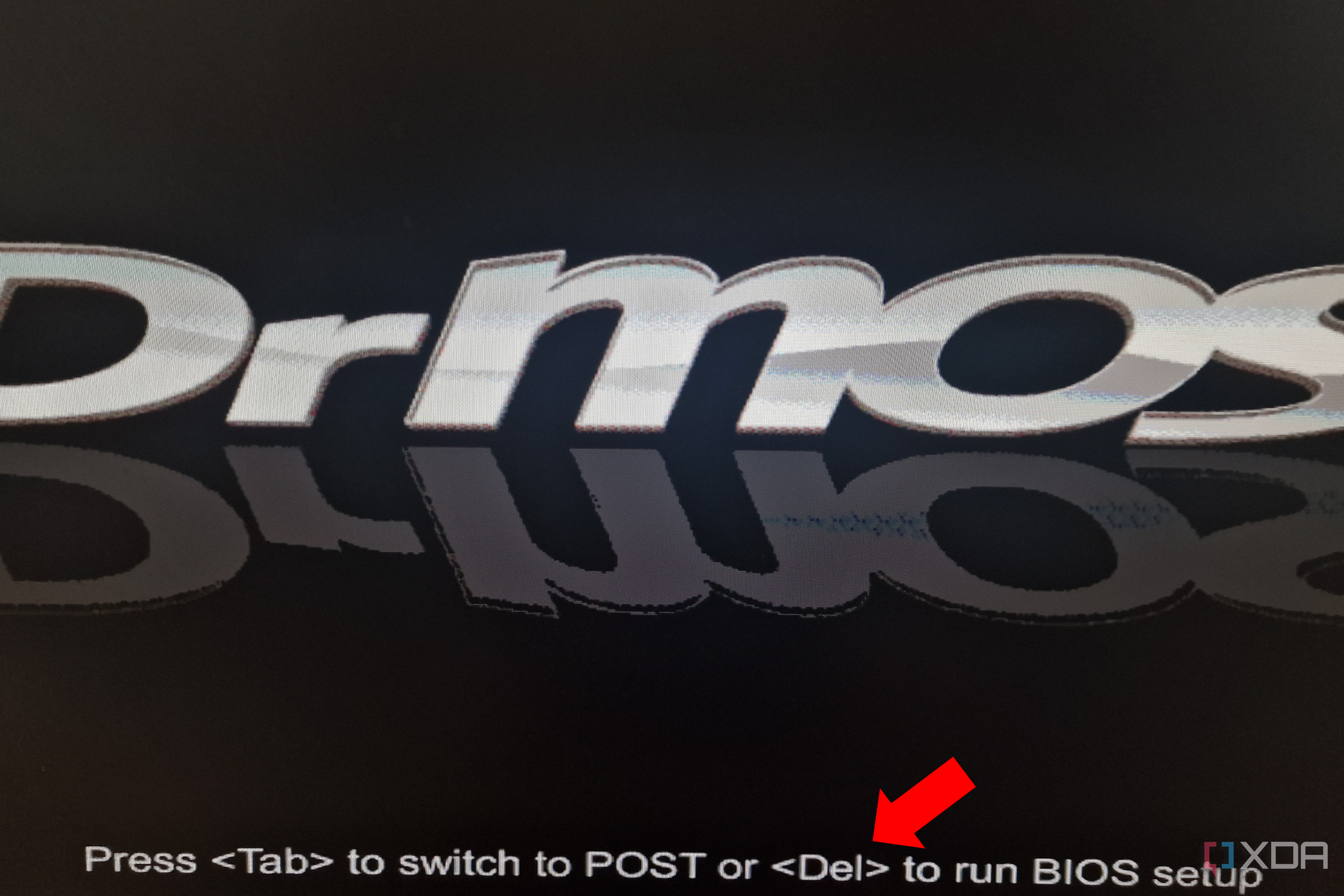 A close-up of a computer screen displaying BIOS boot text "Press <Tab> to switch to POST or <Del> to run BIOS setup" with the BIOS version name partially visible at the top and a red arrow pointing to an option.