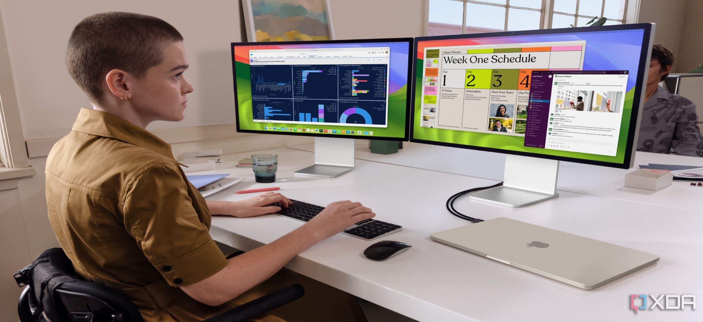 Mujer trabajando con dos monitores grandes y una MacBook Air M3 plateada cerrada