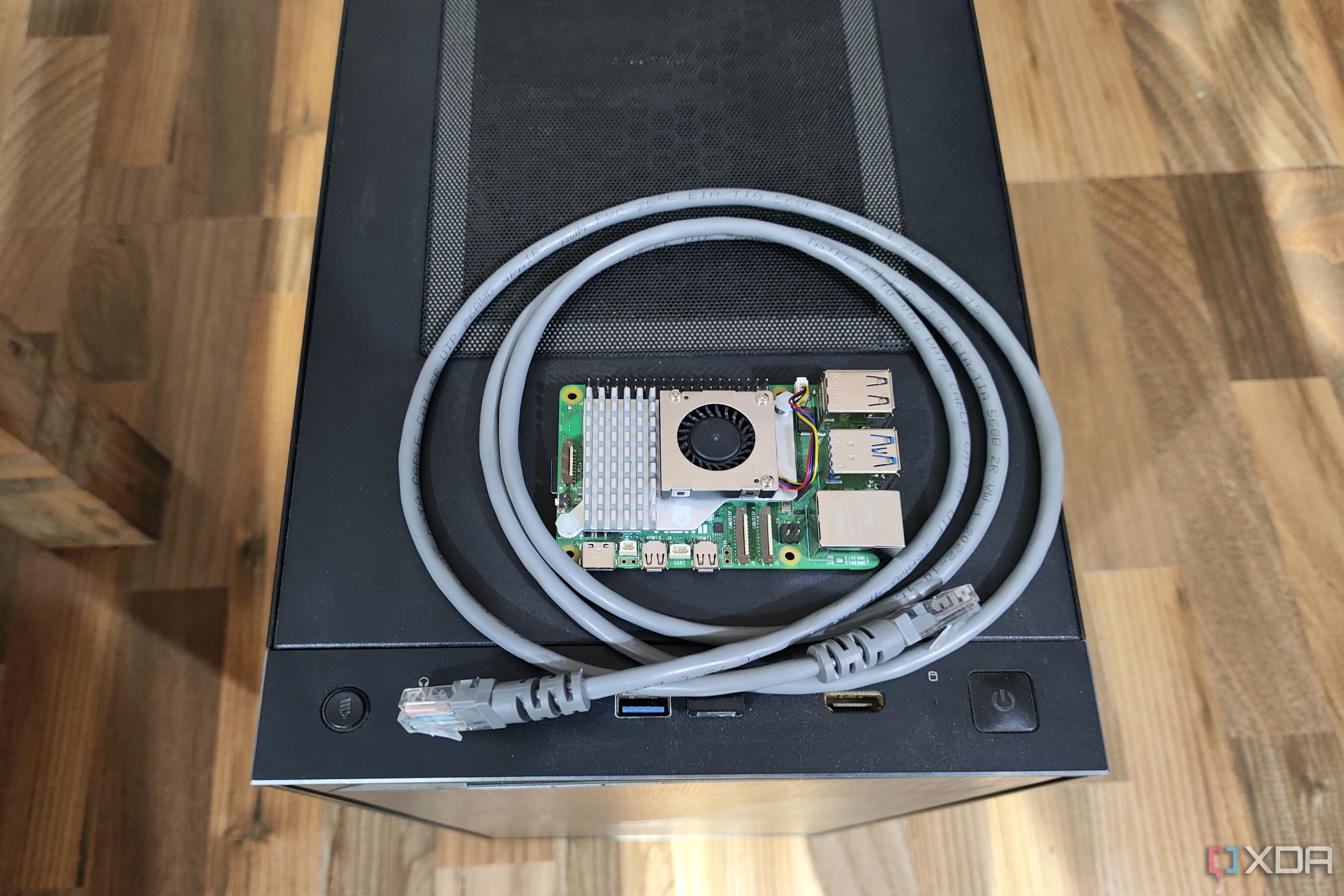A Raspberry Pi 5 resting on a PC case, with a LAN cable wrapped around it