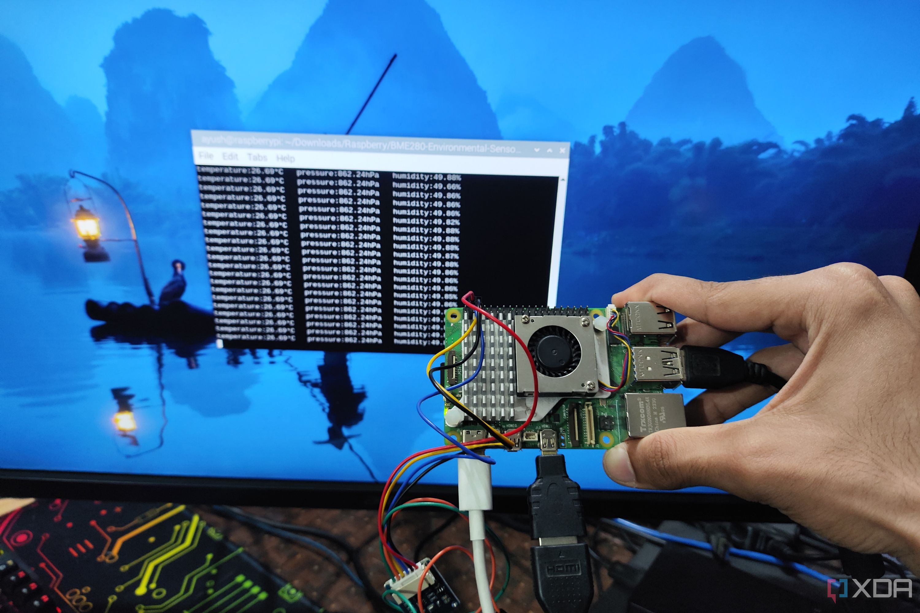 A person holding a Raspberry Pi 5 with a BME280 sensor attached to it in front of a screen