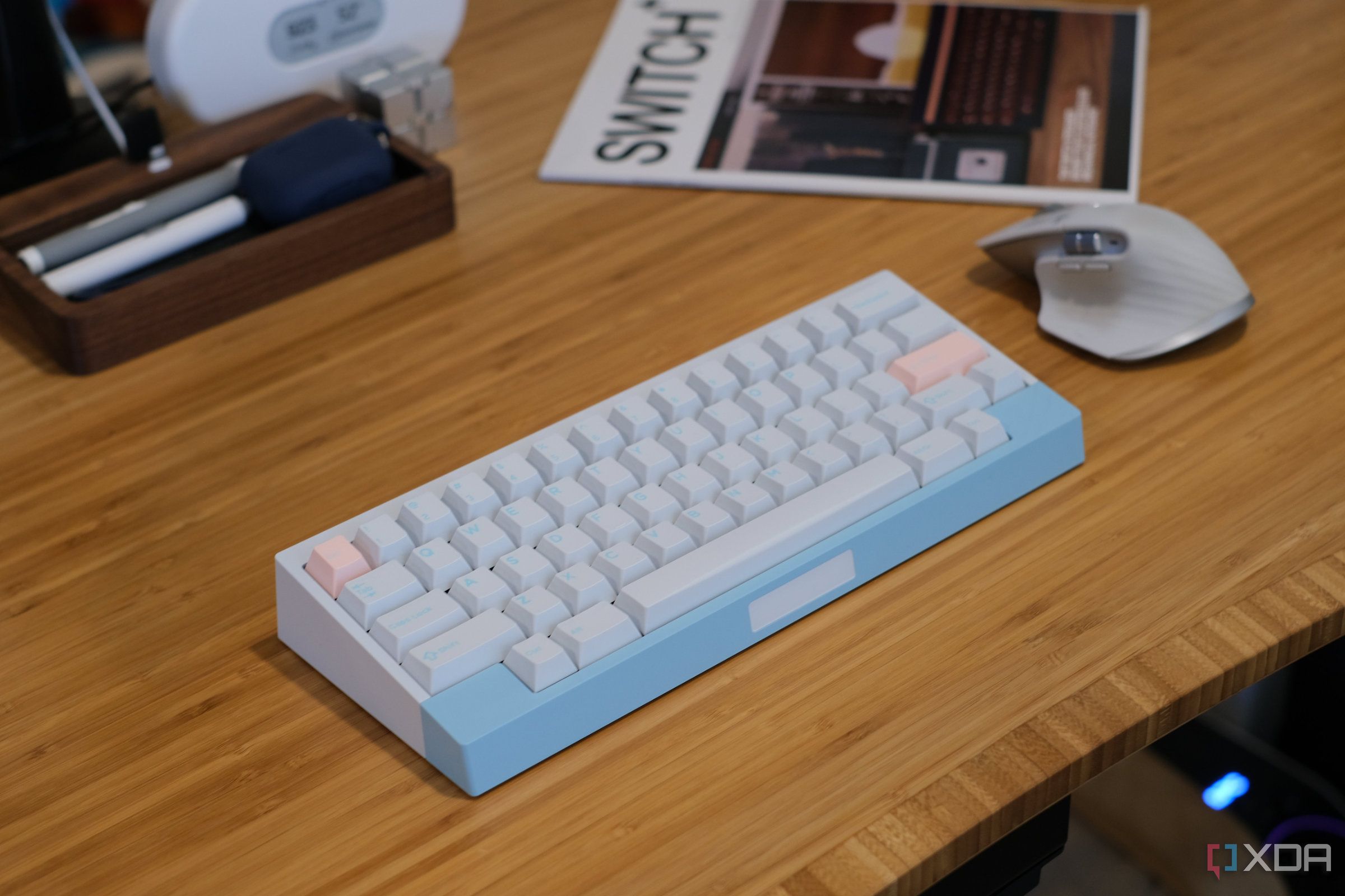 wooden desktop with a compact mechanical keyboard, wireless mouse, keyboard magazine and phone stand on top