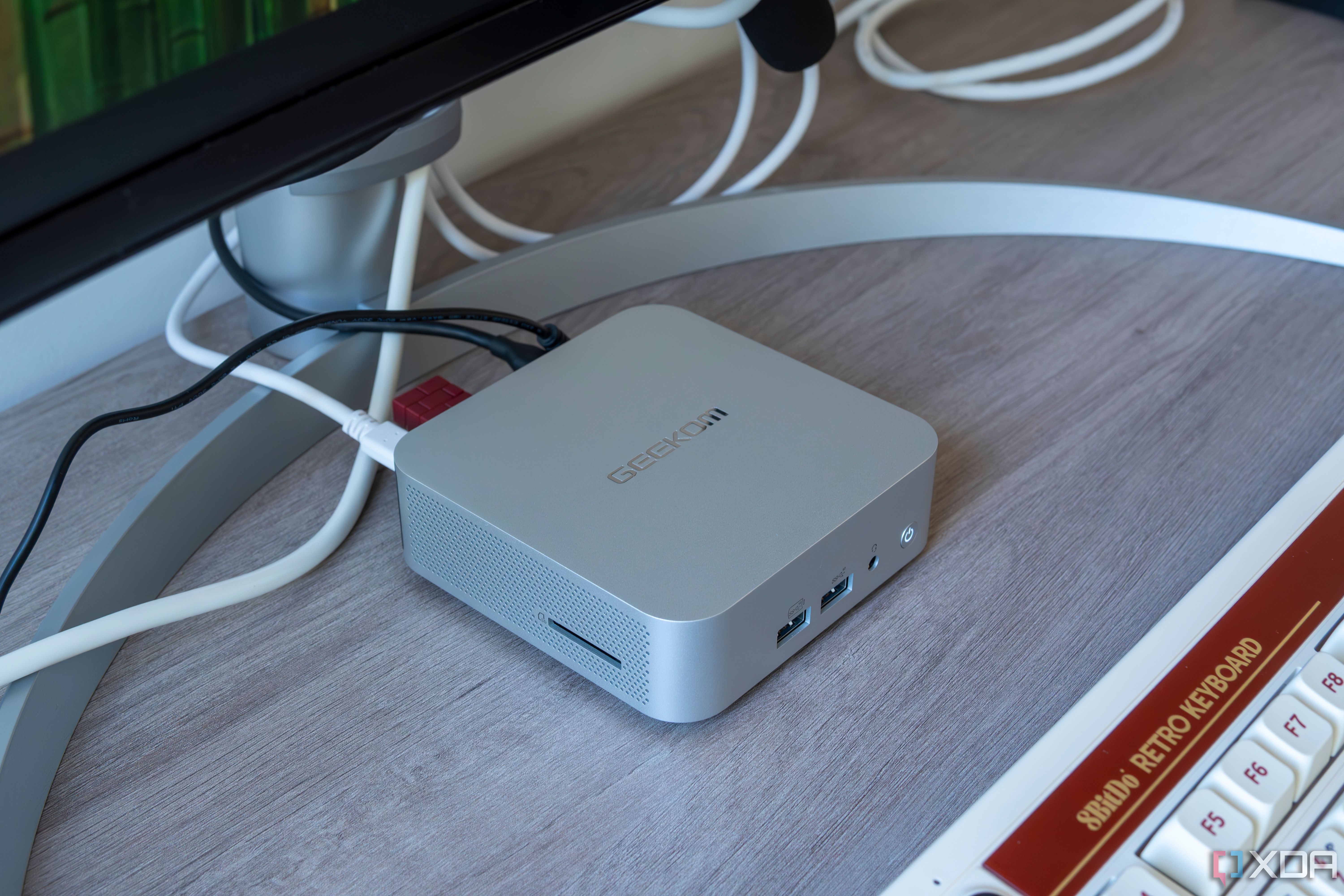 Left-side angled view of the Geekom A8 between a monitor and a keyboard