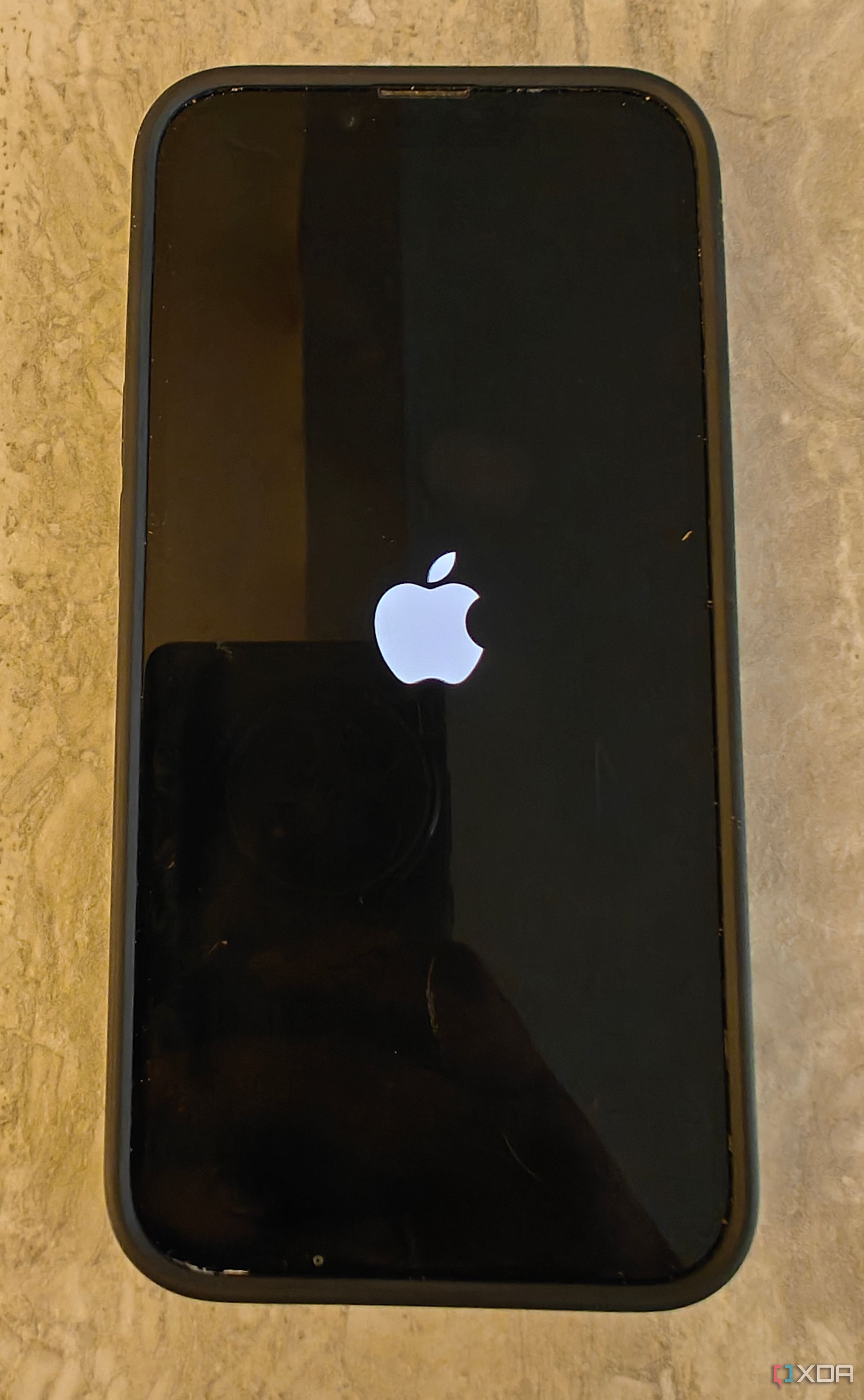 An iPhone on a table with the Apple logo on a black screen.