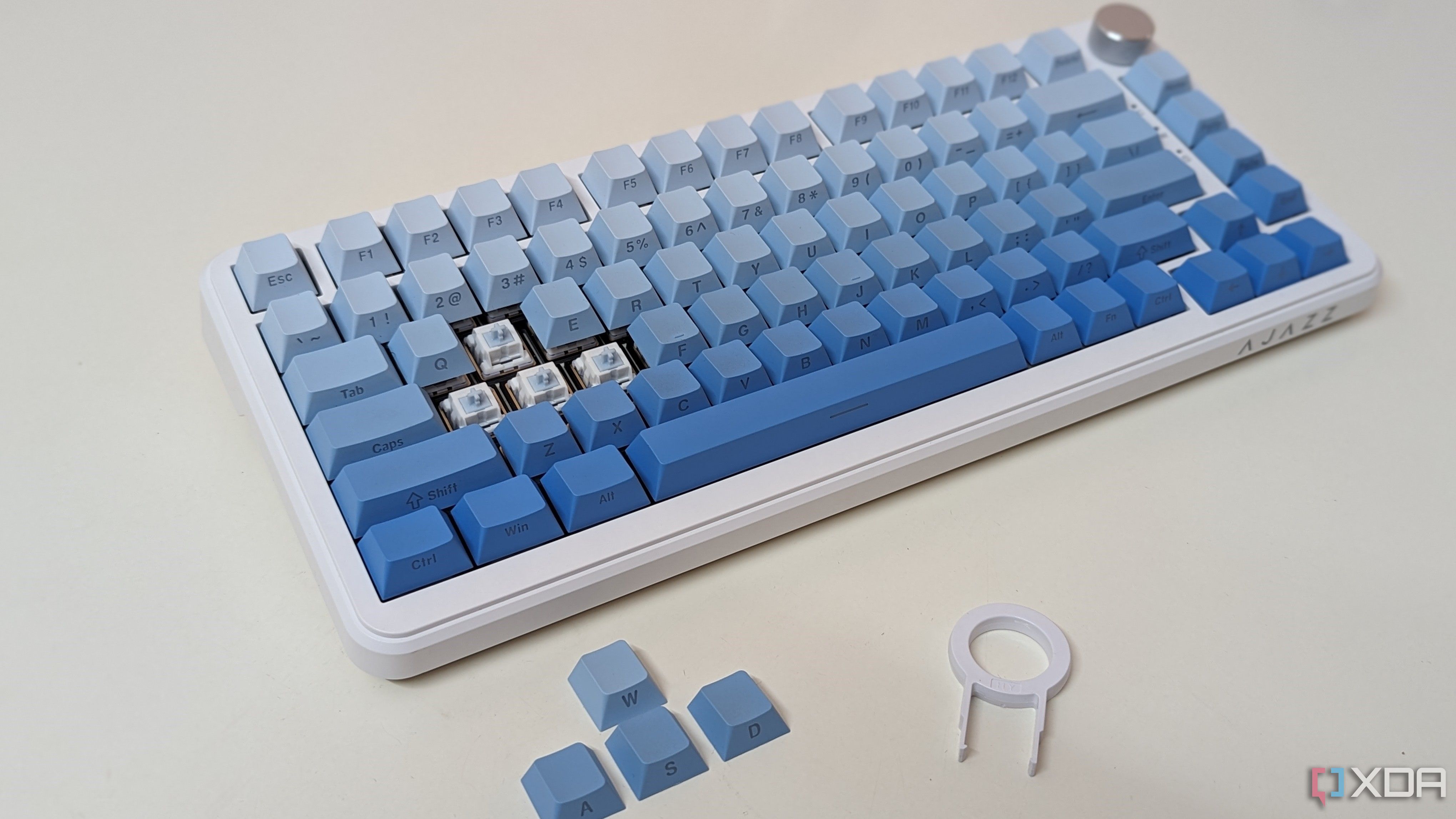 Un teclado azul y blanco sobre una superficie blanca que muestra teclas, interruptores y un extractor de teclas.