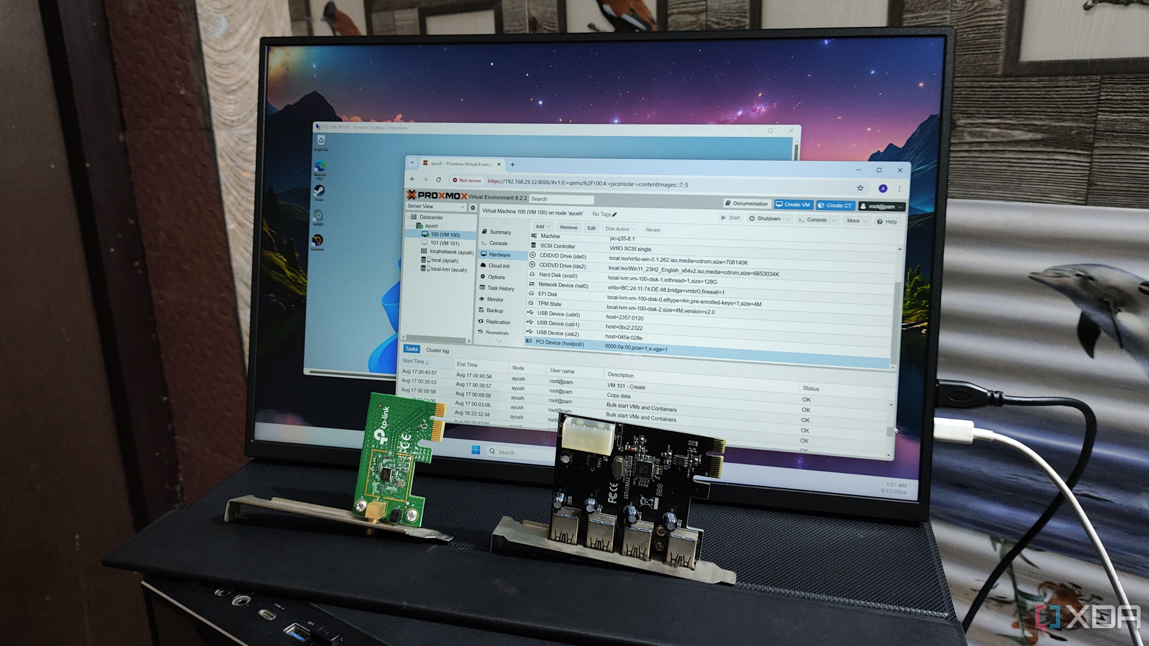 A WLAN card and a USB expansion card kept in front of a monitor displaying the Proxmox UI