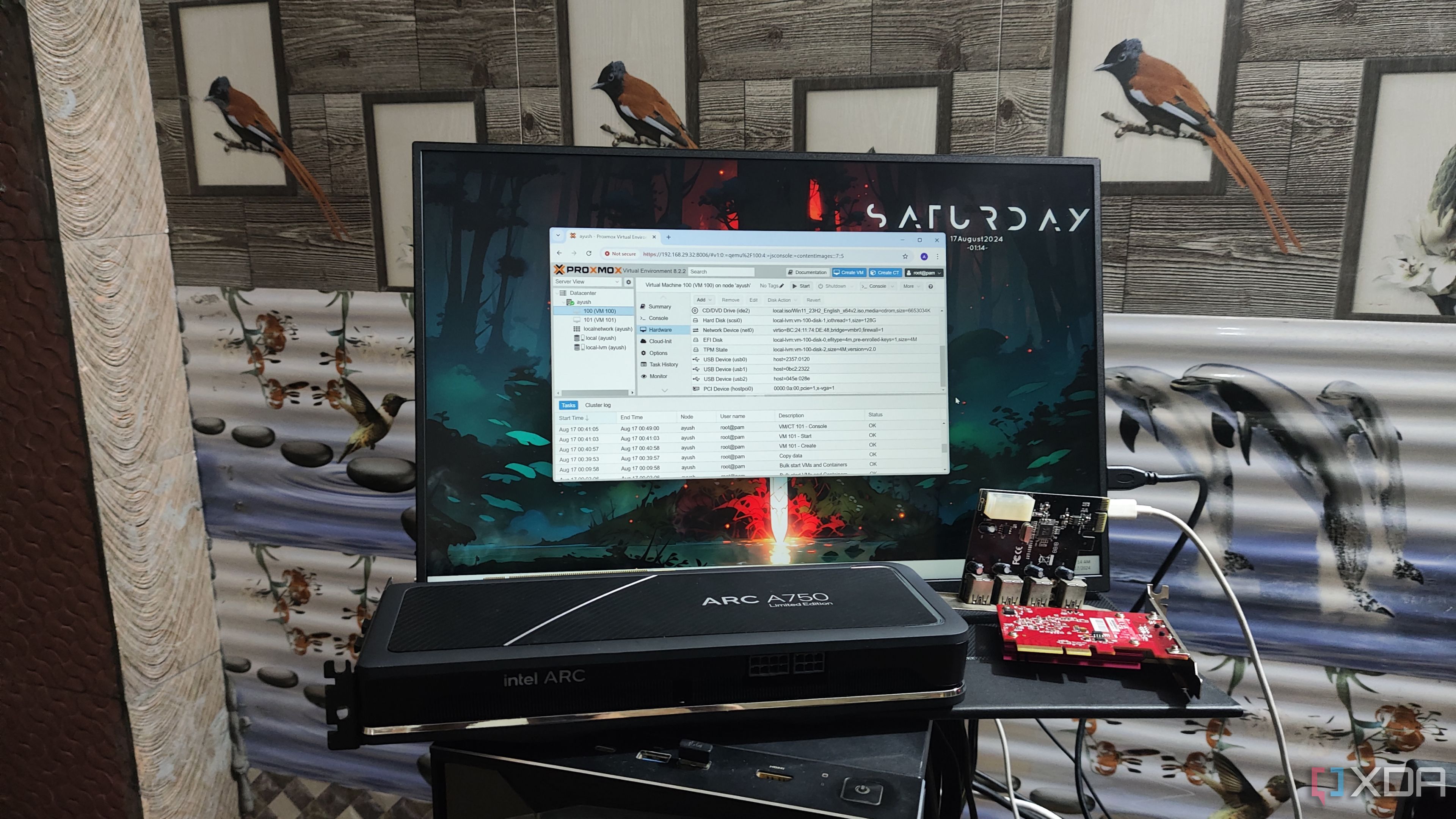 Una GPU Intel Arc A750, una tarjeta WLAN y una tarjeta de expansión USB colocadas frente a un monitor que muestra la interfaz de usuario de Proxmox