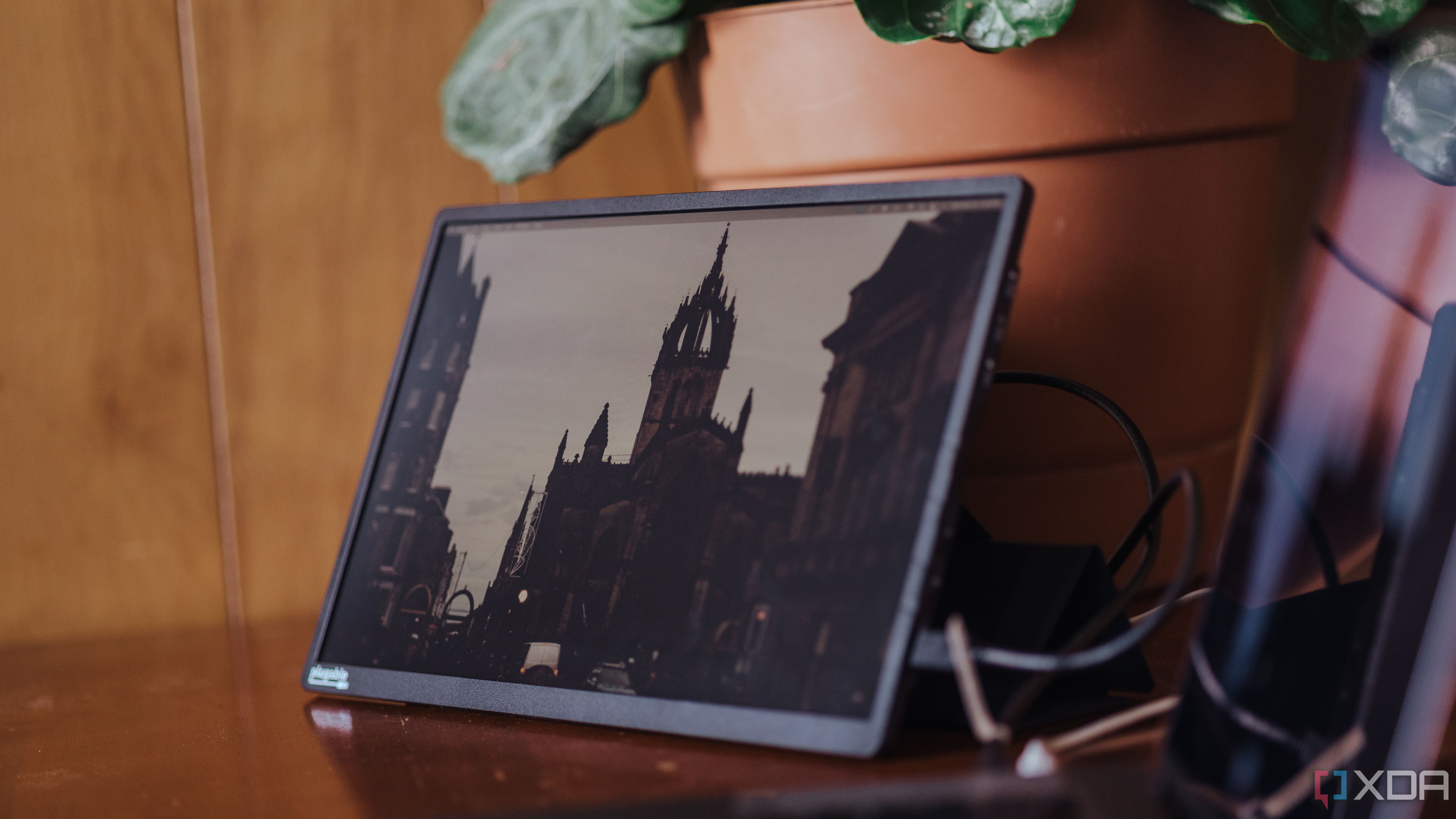 Monitor USB-C portátil enchufable sobre una mesa de madera frente a una planta