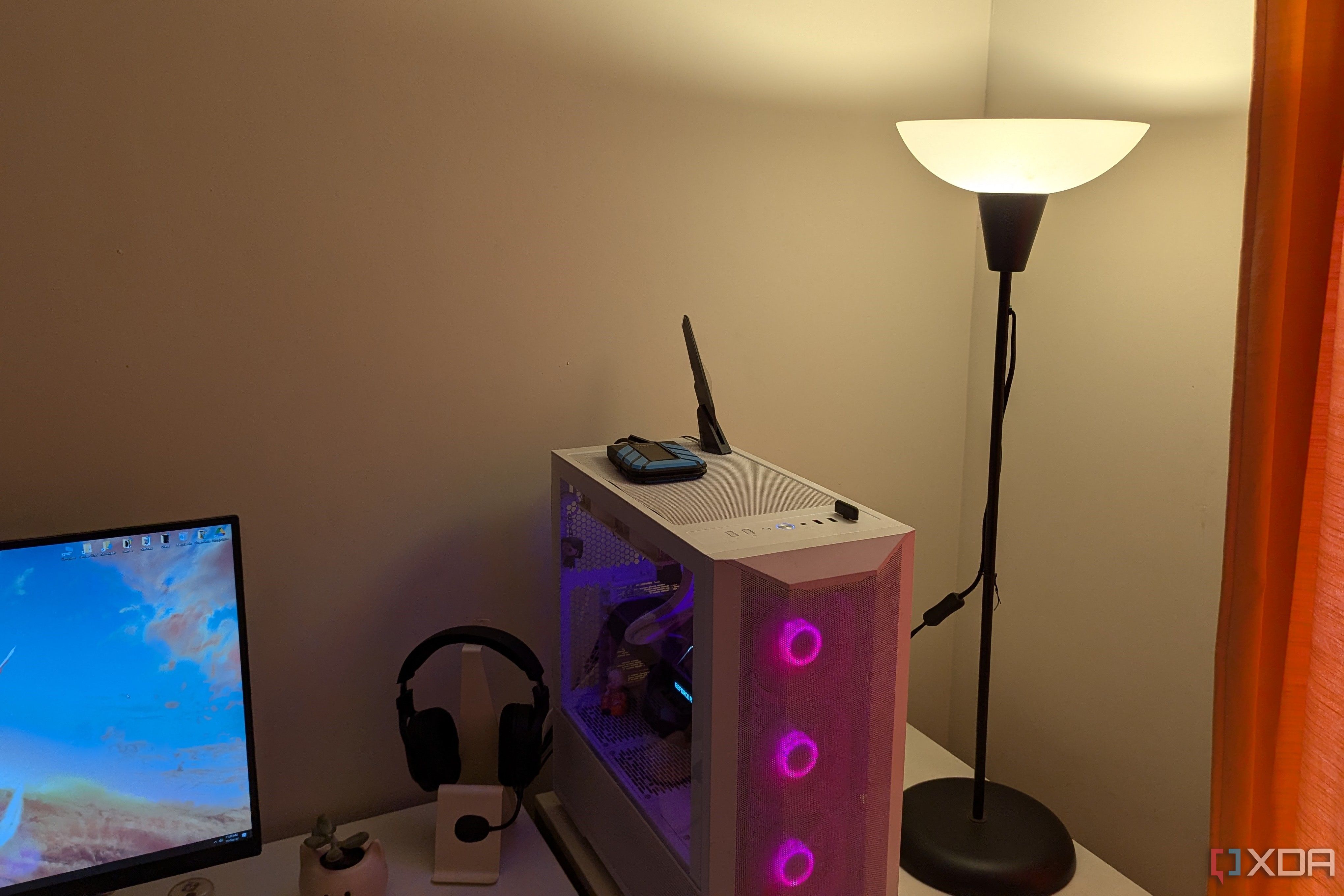 Una lámpara de iluminación cálida junto a una PC para juegos y un escritorio blanco.