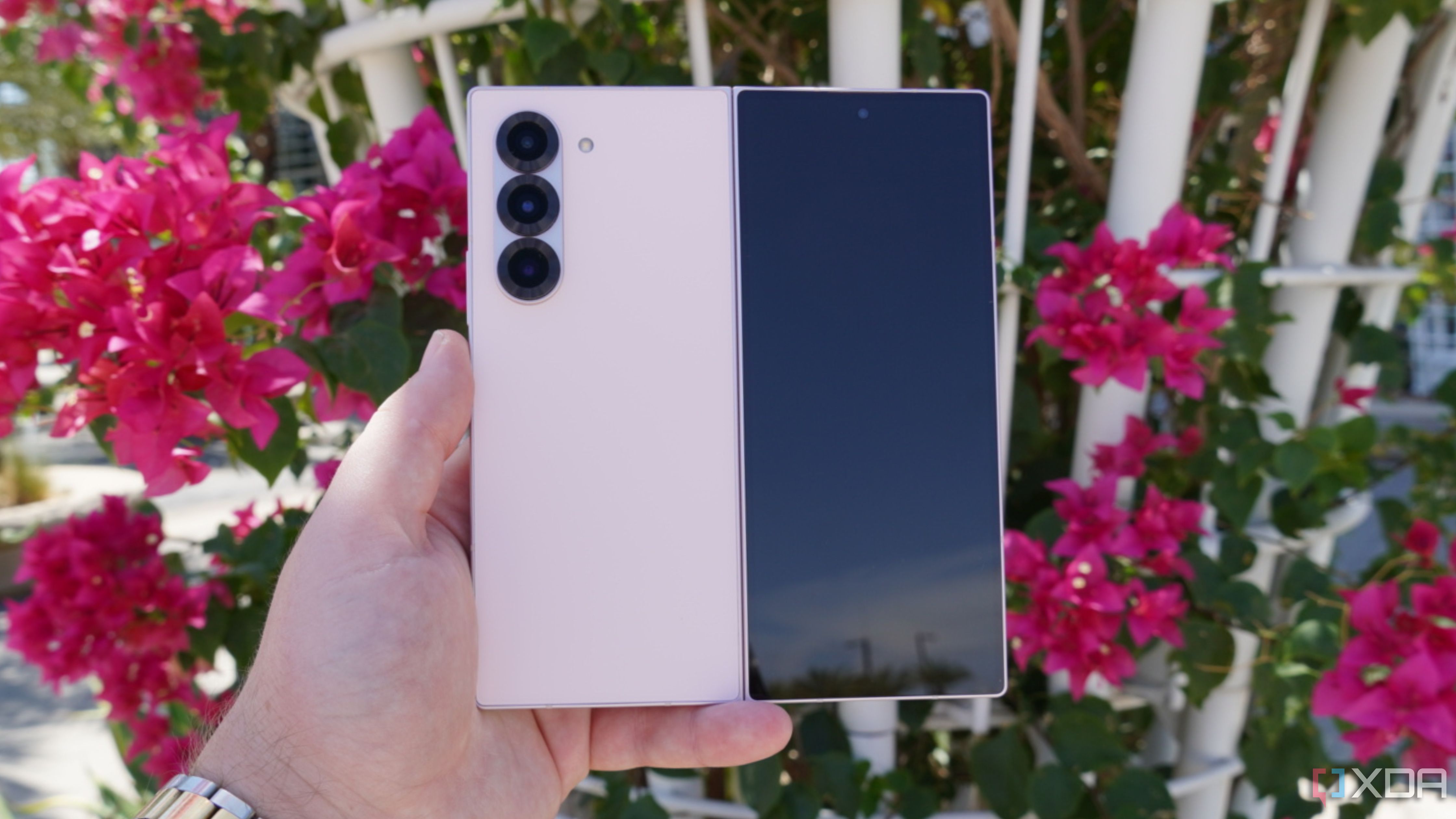 The pink Samsung Galaxy Z Fold 6 in the hand in front of flowers.