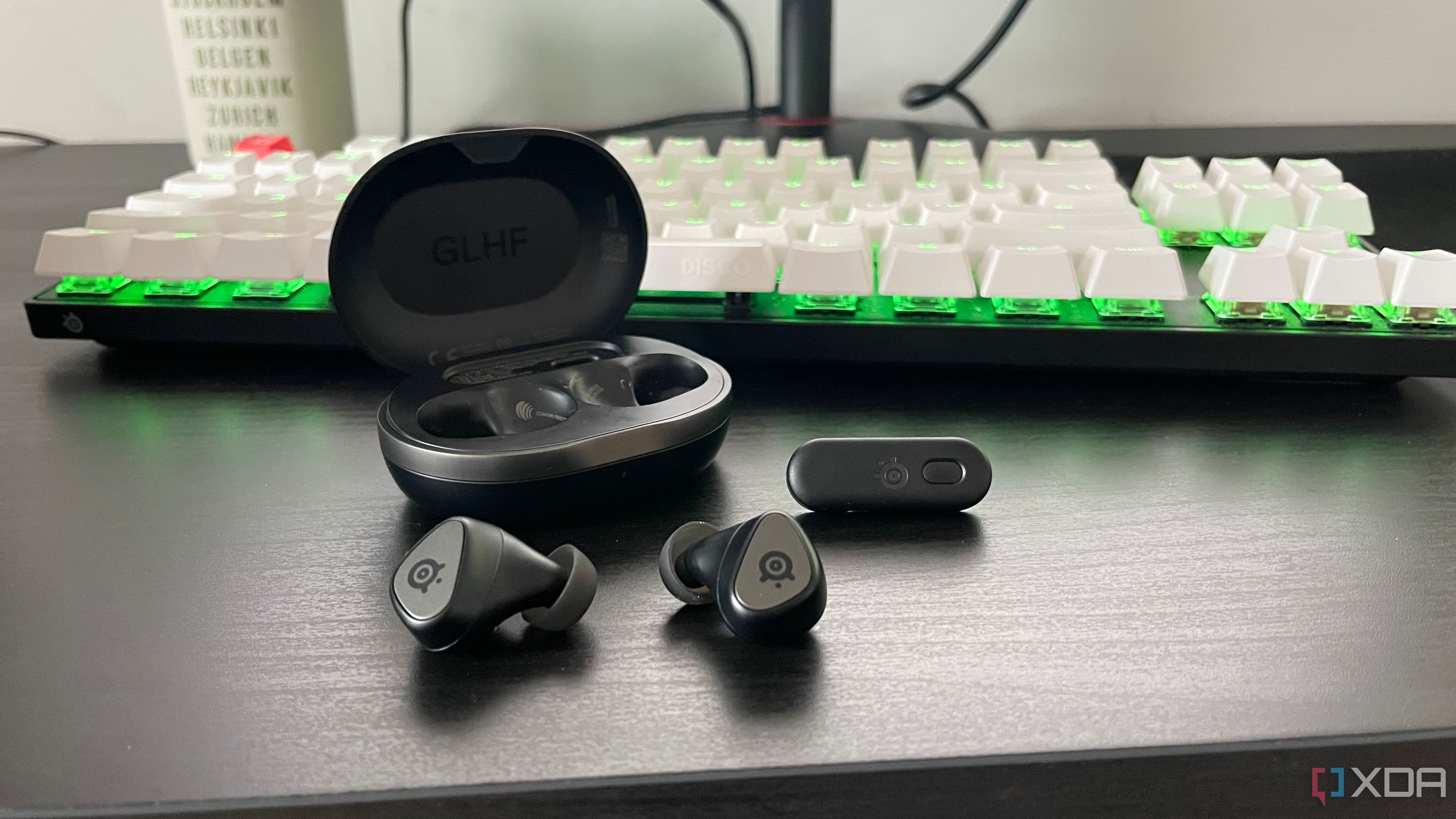 Los SteelSeries Arctis GameBuds exhibidos fuera de su estuche frente a un teclado mecánico para juegos.