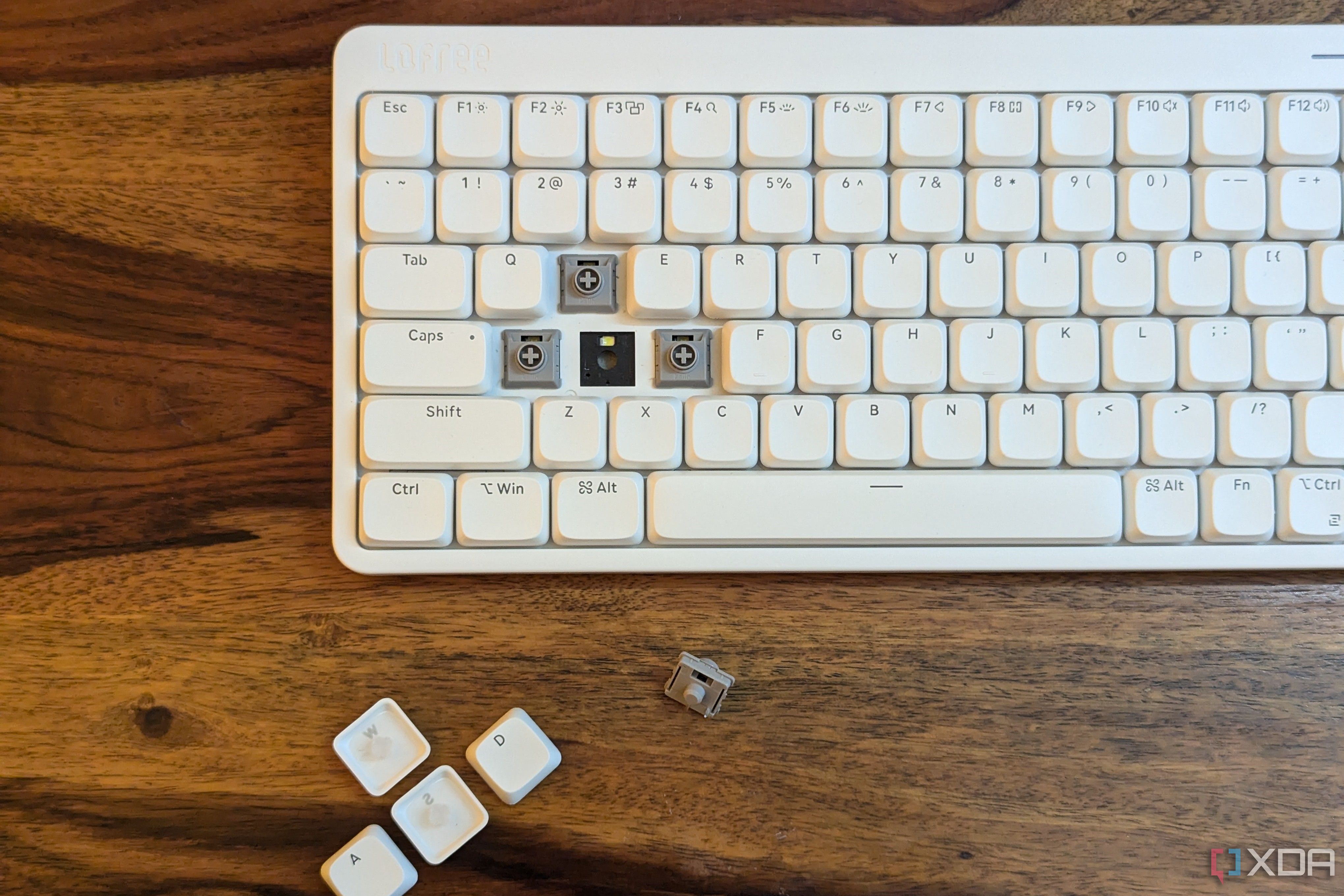 Un teclado mecánico blanco de perfil bajo con teclas y un interruptor quitados