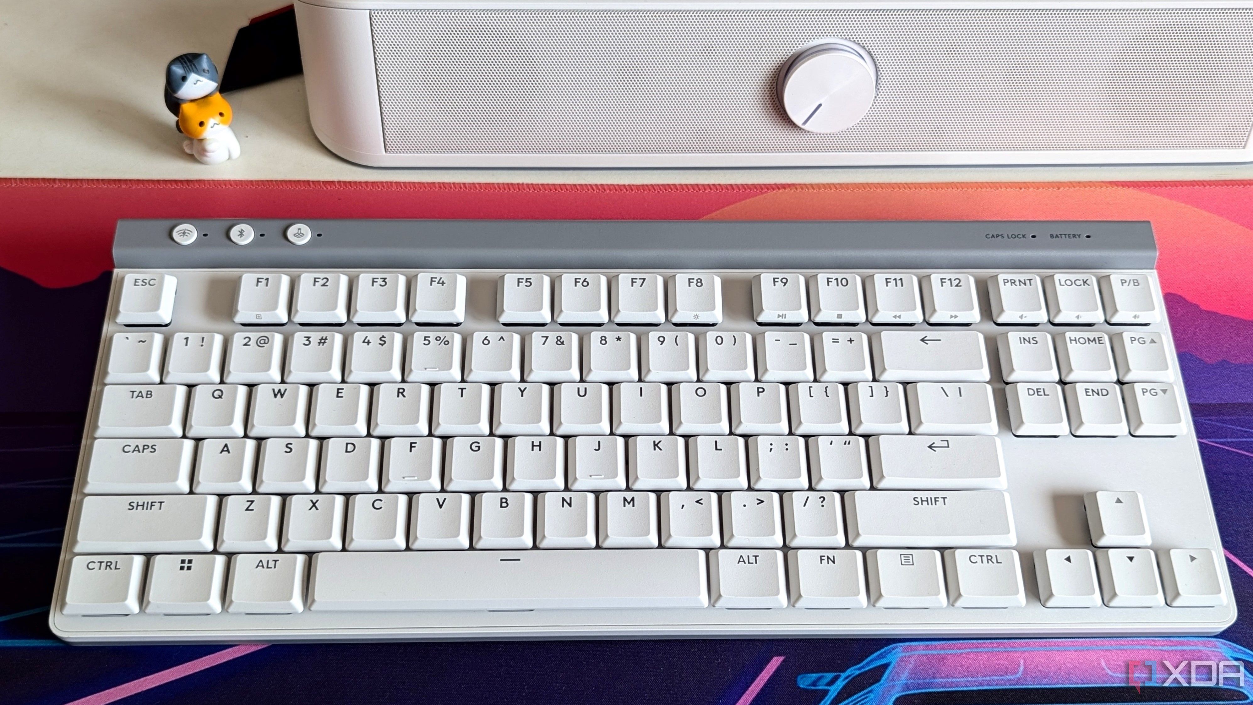 Vista superior de un teclado mecánico blanco junto a una barra de sonido en un escritorio