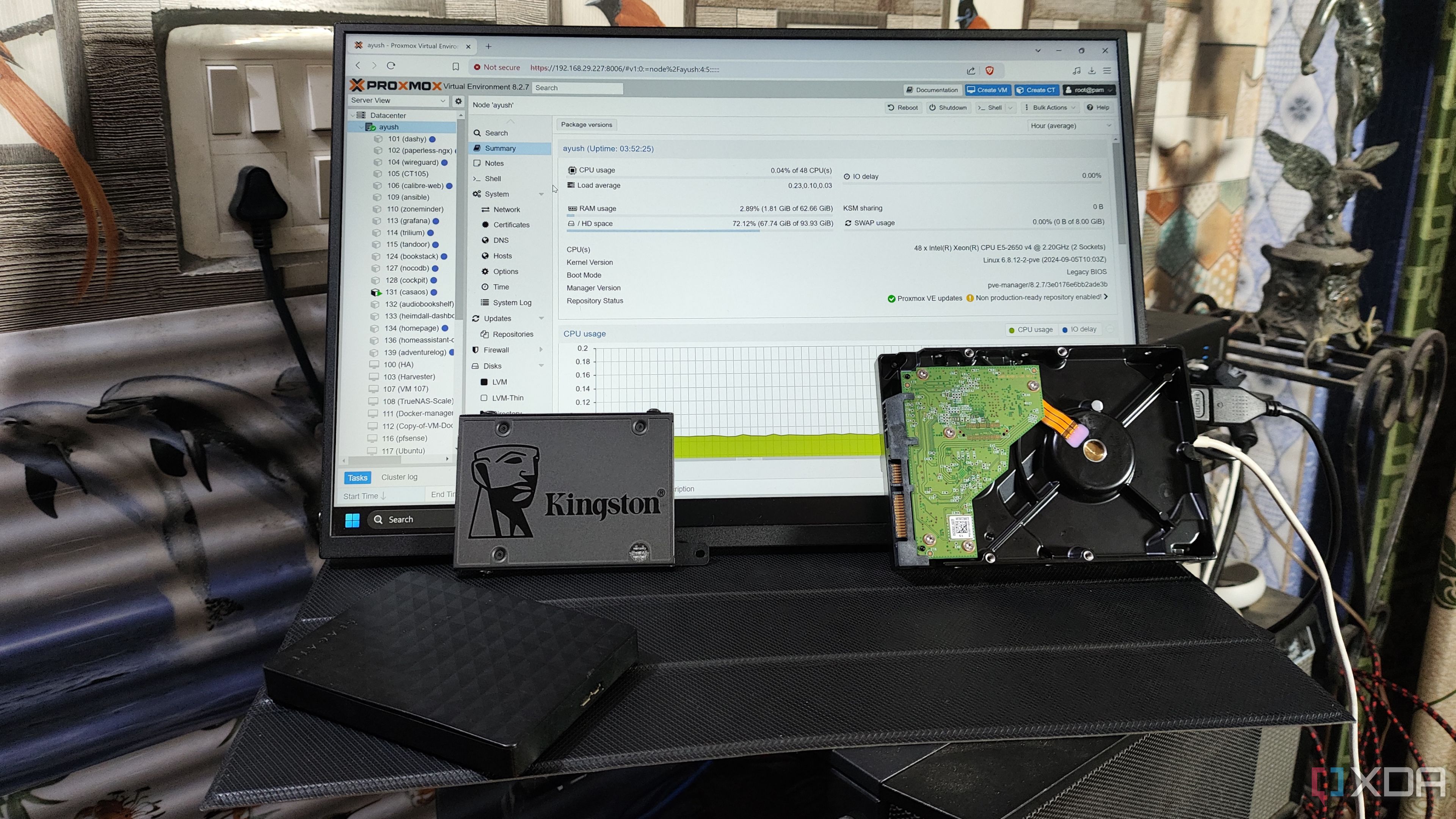 Algunos discos duros y un SSD Kingston colocados frente a un monitor que muestra la interfaz web de Proxmox