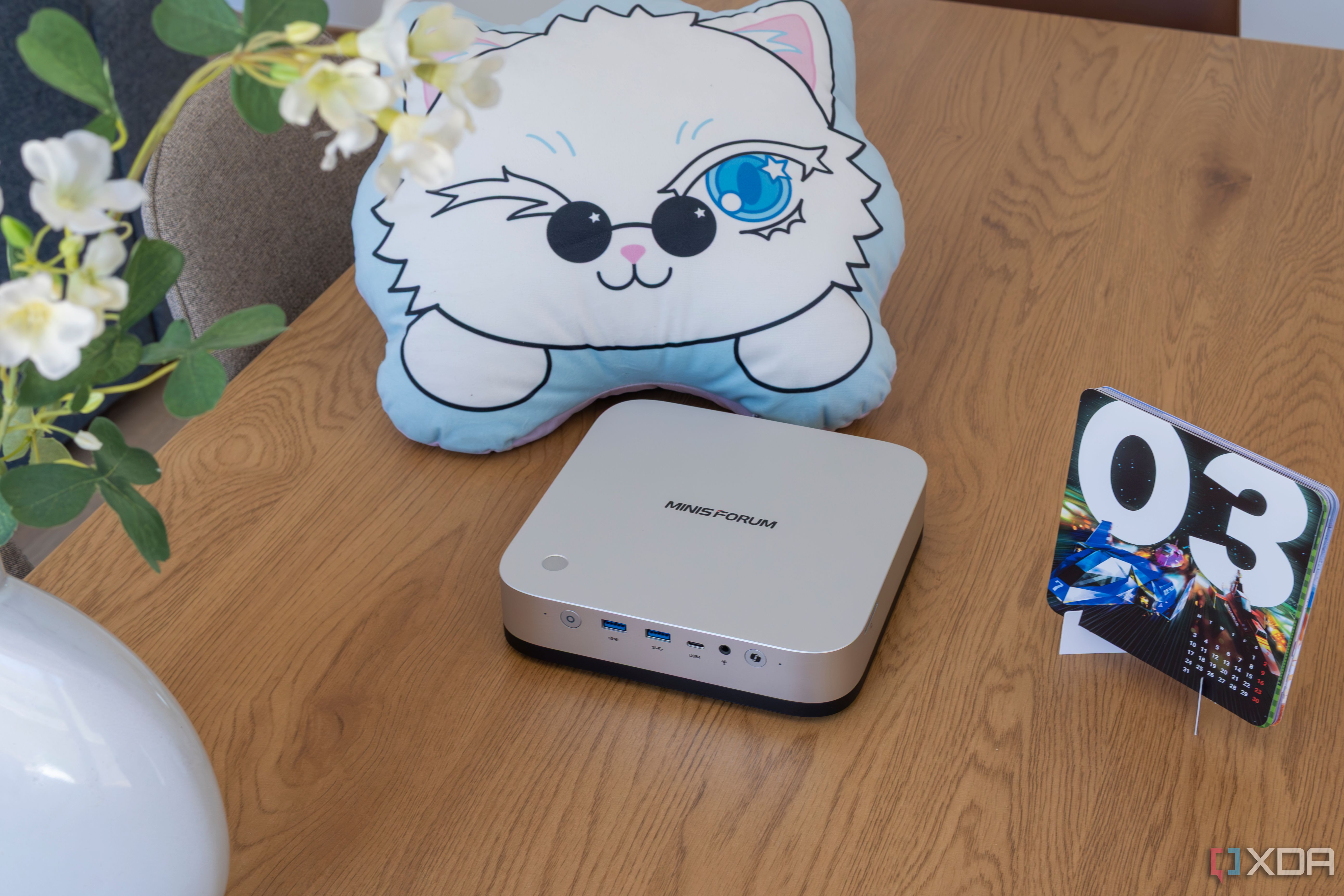 Angled view of a Minisforum AI X1 Pro on a wooden table next various other objects