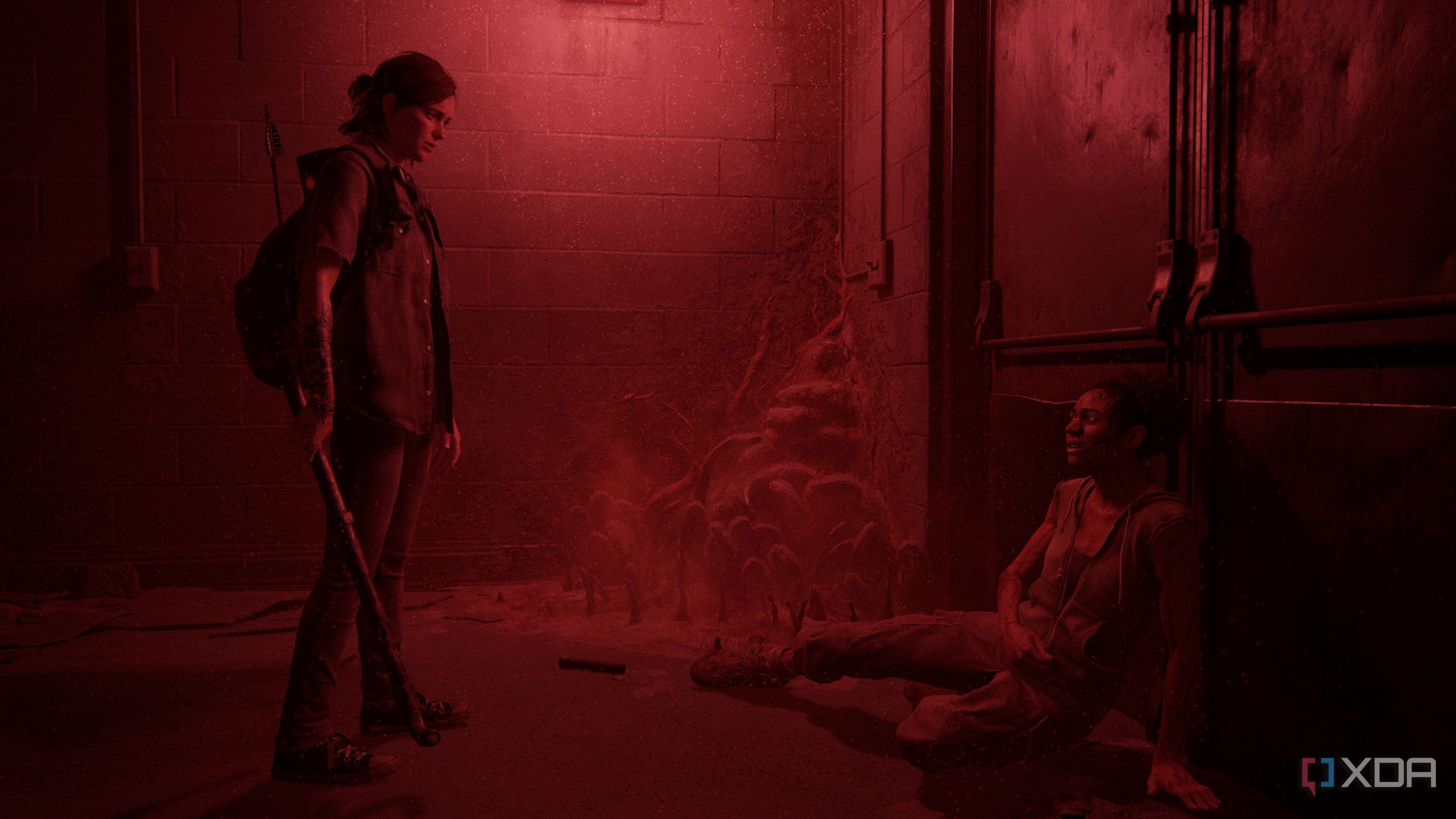 Ellie standing over Nora in a dark, red-lit hallway in The Last of Us Part II.