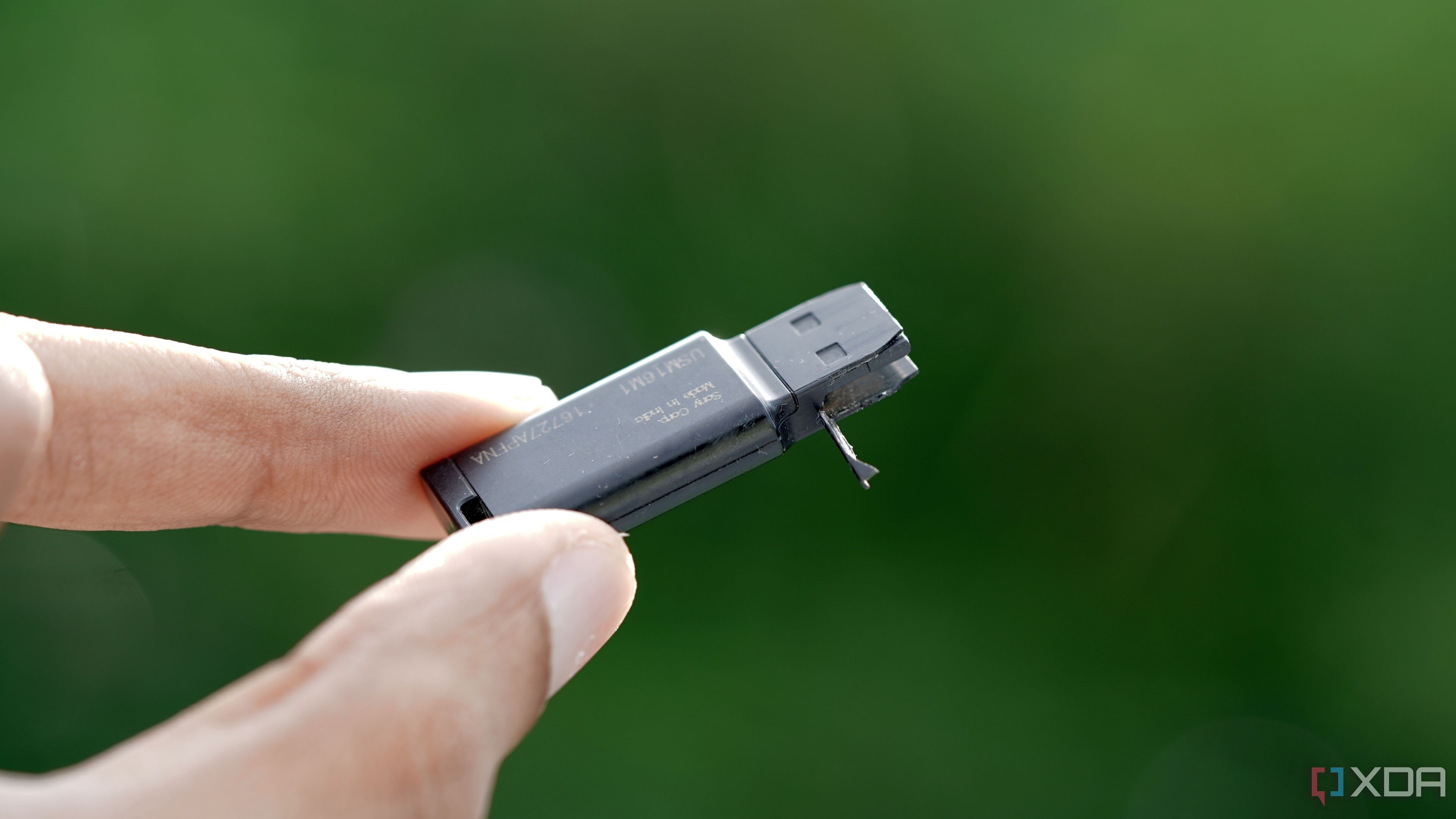 A chewed up black Sony 16GB USB flash drive against a lush green foliage